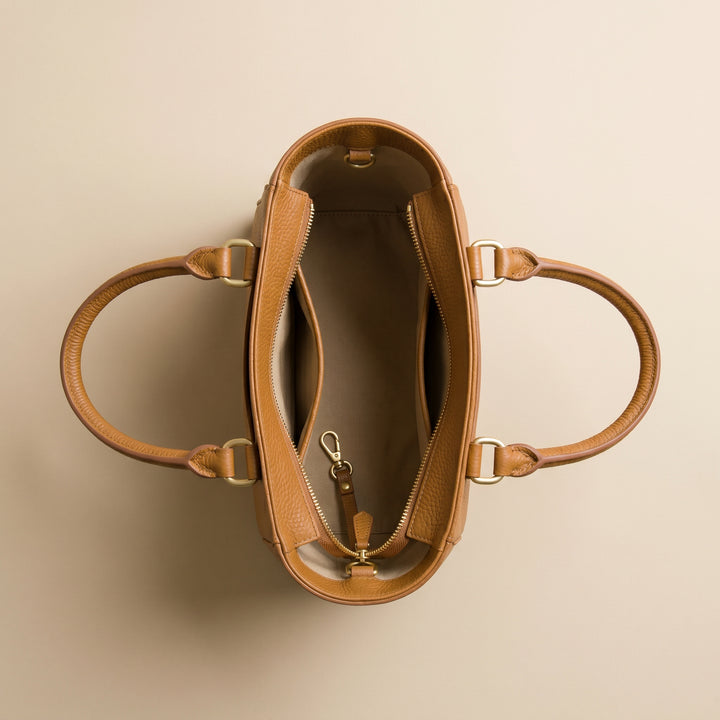 Brown leather handbag with gold hardware on a beige background